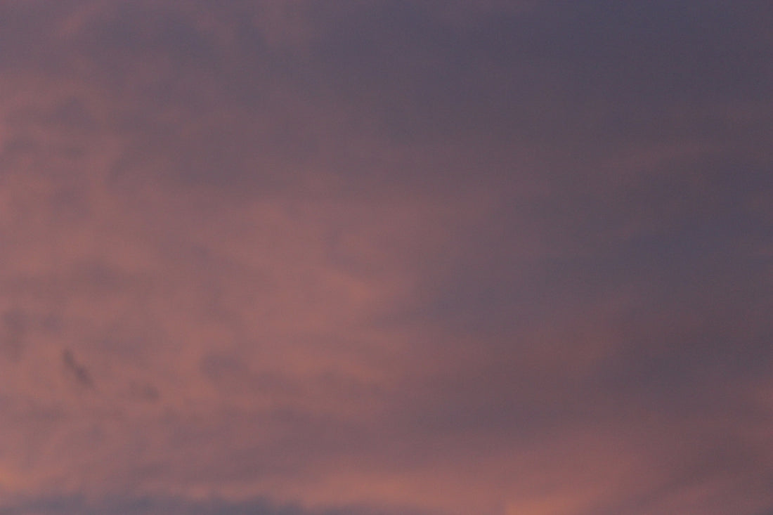 a plane flying through a cloudy sky at sunset