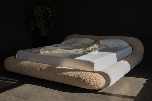 Modern bed with rounded headboard and white linens.