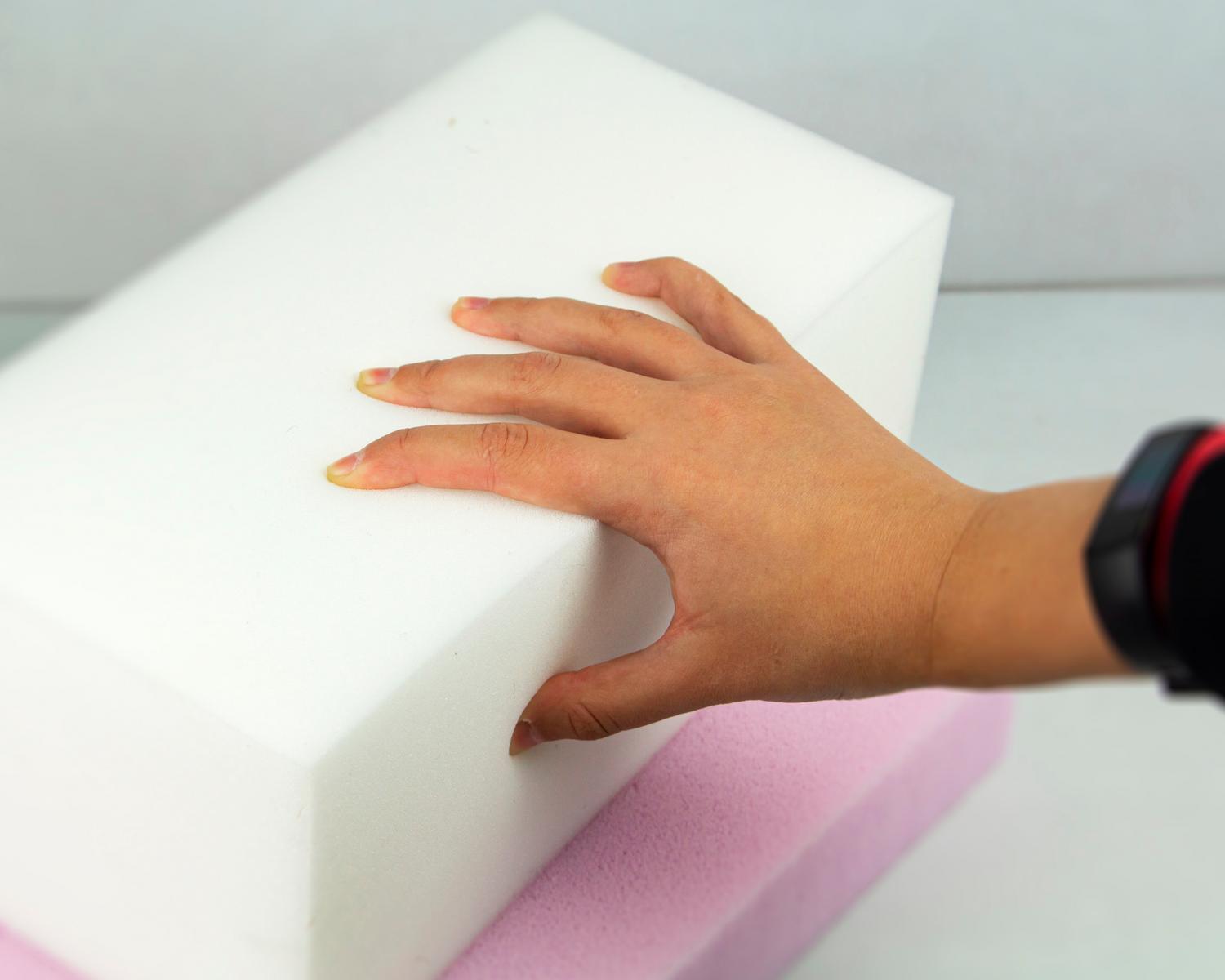 Close-up of a hand pressing into a block of Reflex foam, showcasing its firm and springy properties.