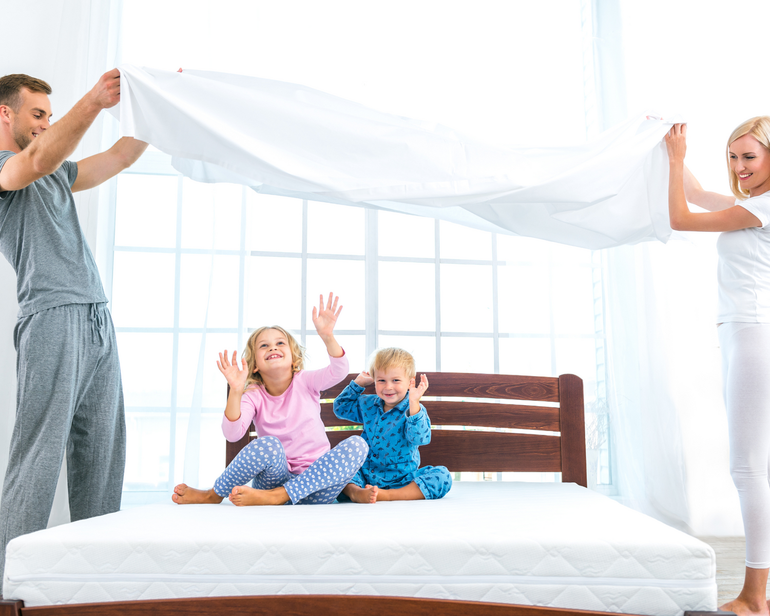 A family of four messing around on a bed.