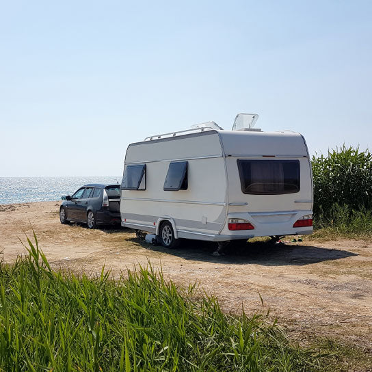 Image of a car with a touring caravan attached, parked near the edge of a breath-taking remote beach, showcasing the beauty and tranquillity of caravan holidays.