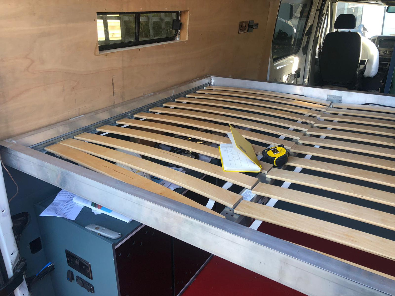 Custom aluminum bed frame designed to perfectly fit a mattress inside a campervan, featuring a sleek and sturdy metal construction for a snug and secure mattress placement, optimizing space in a compact living environment.