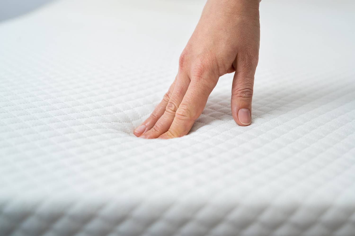 Close-up of a hand pressing into a mattress surface to test its firmness, emphasizing the mattress's supportive qualities.