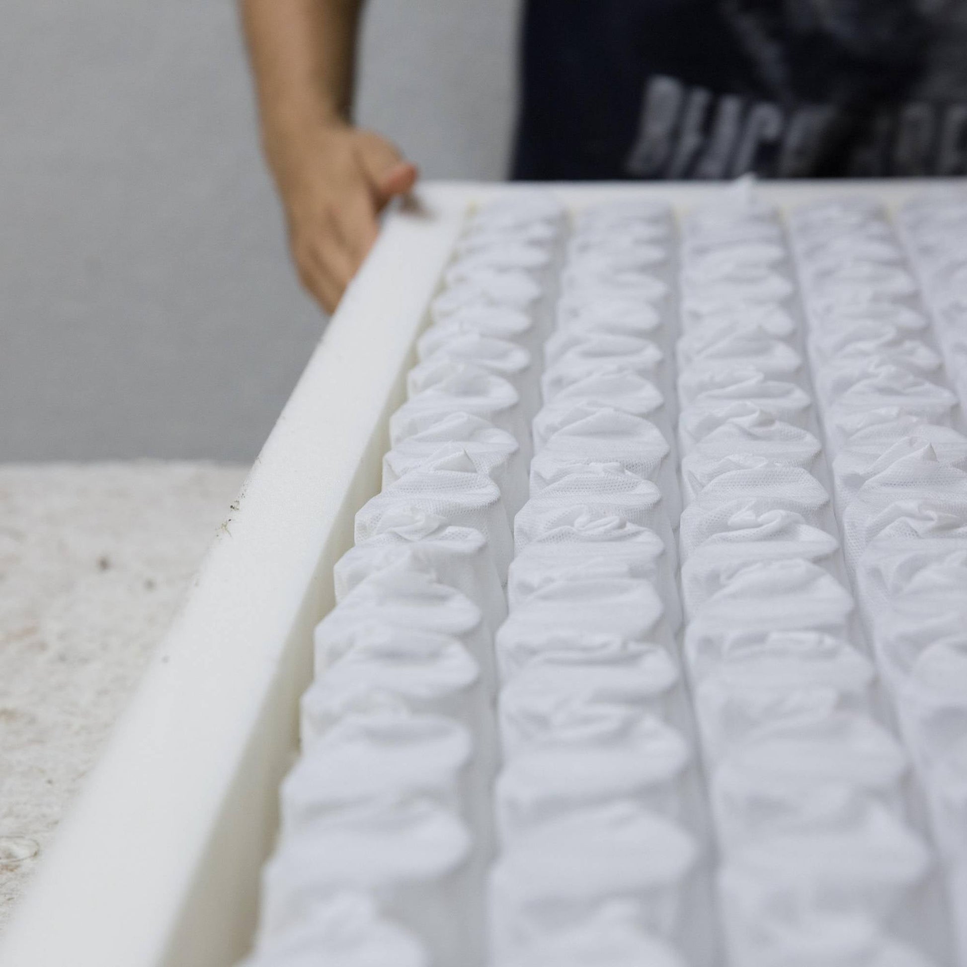 A craftsman hand-assembles a Hybrid Caravan Mattress, featuring a foam-encapsulated border and visible pocket springs, on a worktable.