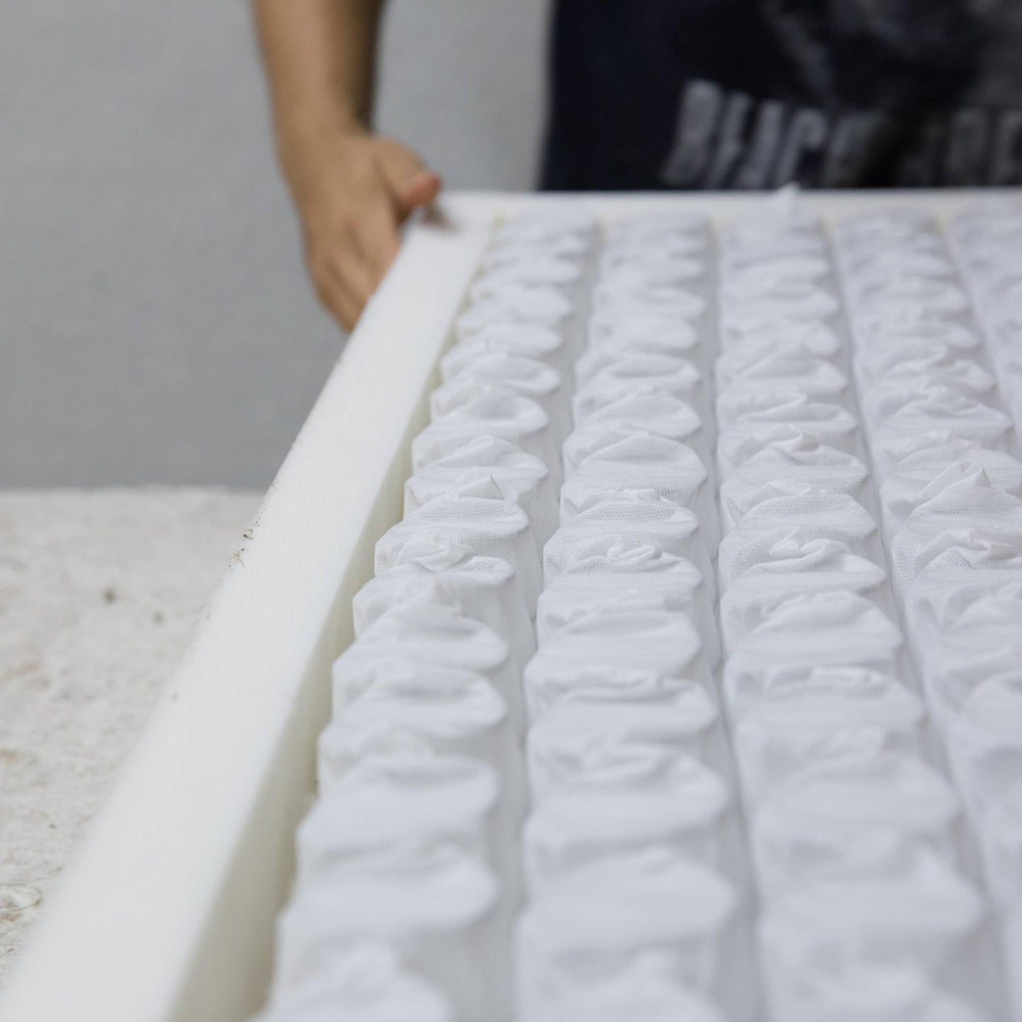 A craftsman hand-assembles a Hybrid Caravan Mattress, featuring a foam-encapsulated border and visible pocket springs, on a worktable.