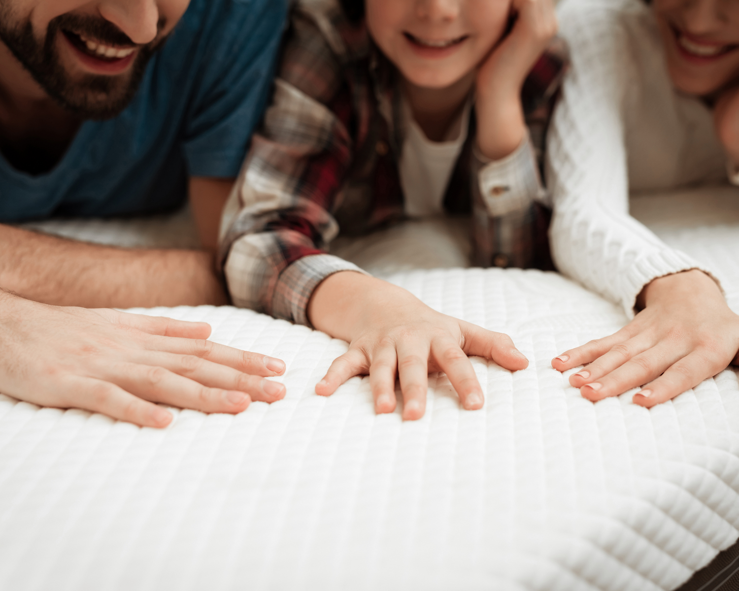 Family of various ages lying together on a bed, each touching the made-to-measure mattress, illustrating its long-lasting quality and suitability for all life stages.