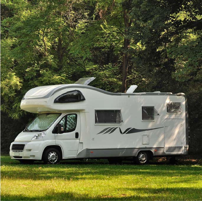 Image of a motorhome comfortably parked in a scenic grass field, with a lush forest serving as the perfect backdrop to this idyllic setting.
