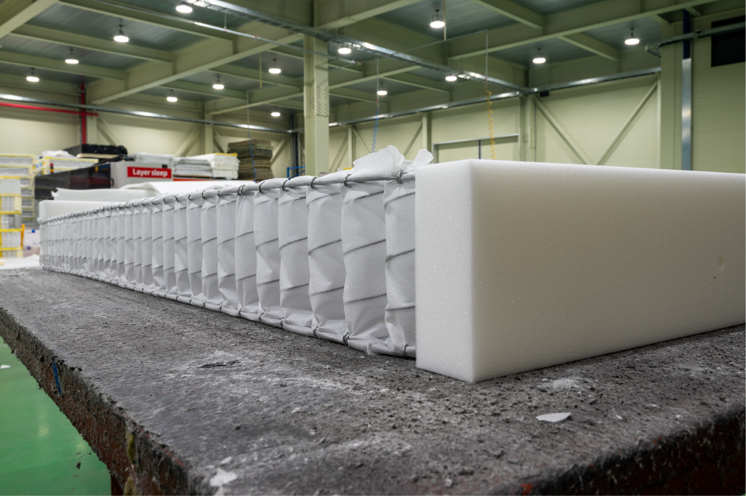 Side view of pocket springs encased in foam on a workbench, highlighting the depth and layering of the mattress's internal structure.