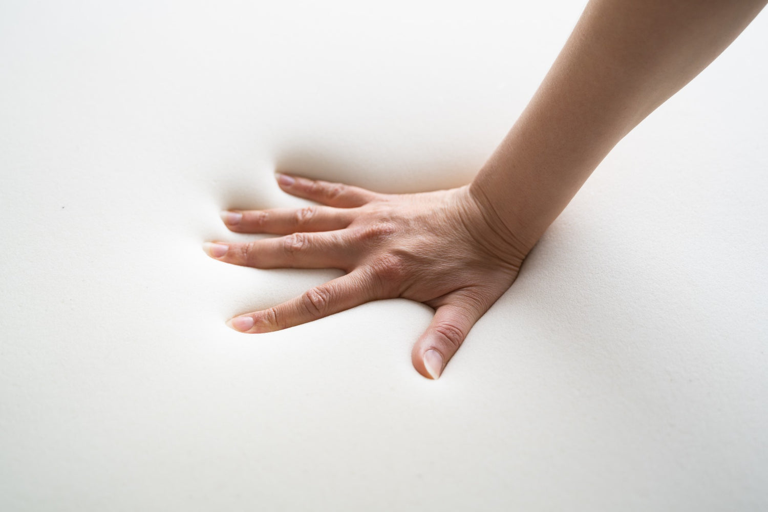 Hand pushing into a slab of memory foam leaving an impression