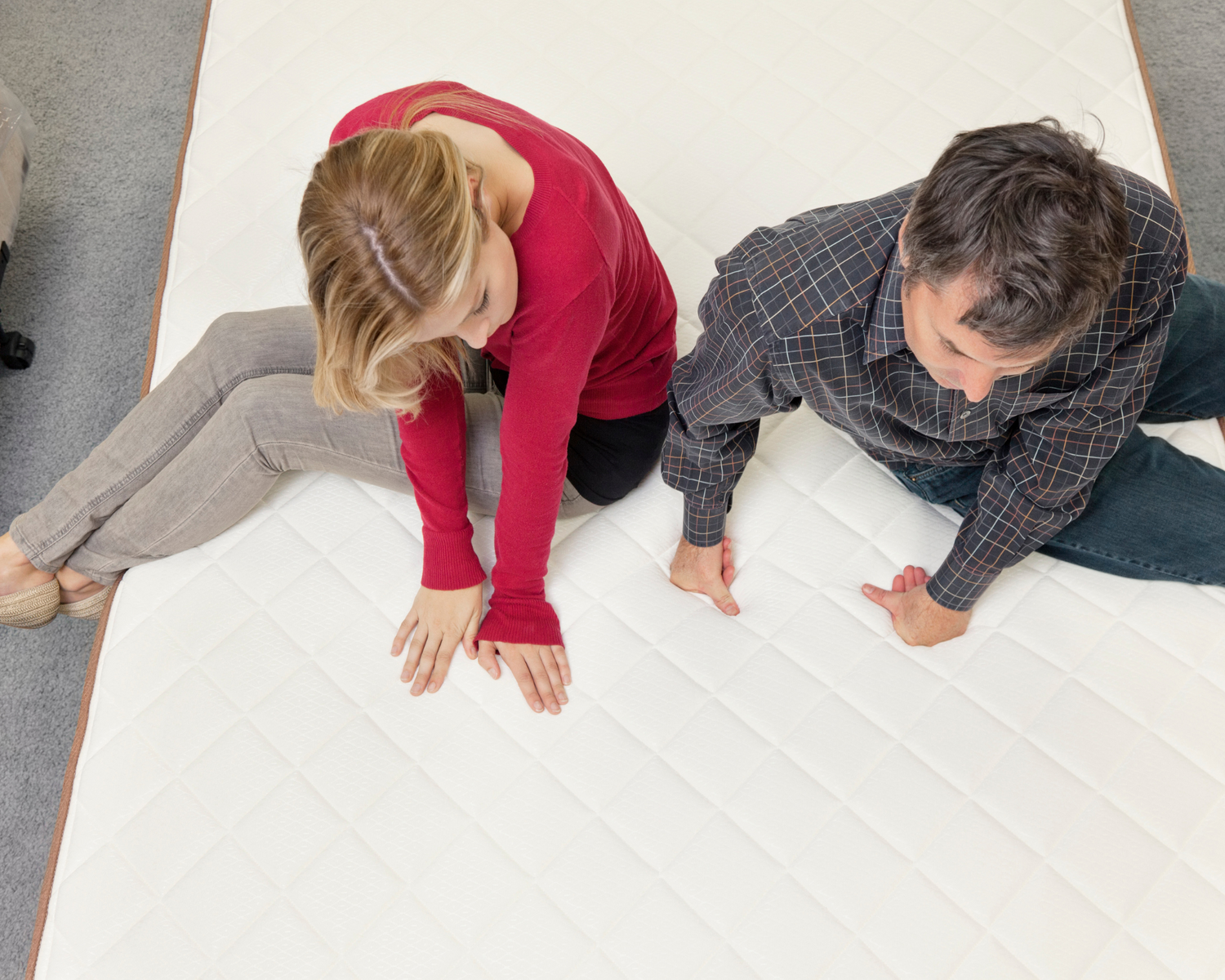Two people sitting on the same mattress deciding if its the correct firmness